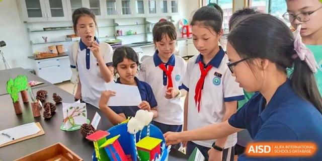 Wenzhou Union International School (WUIS) students, including one wearing a Young Pioneer scarf, collaborating on a hands-on experiment with colorful objects and water.