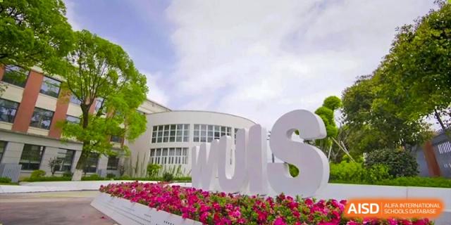 A close-up of the Wenzhou Union International School (WUIS) logo sculpture on the campus surrounded by pink flowers.