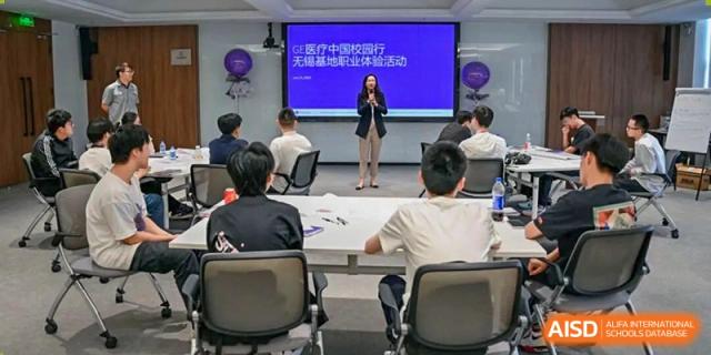 A female teacher or speaker presenting a lecture to students in a classroom with a large screen displaying Chinese text at Wuxi No.1 High School.