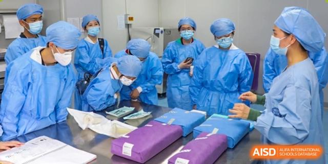 Students wearing surgical gowns and caps in a simulated operating room or medical lab, examining sterilized packages at Wuxi No.1 High School.