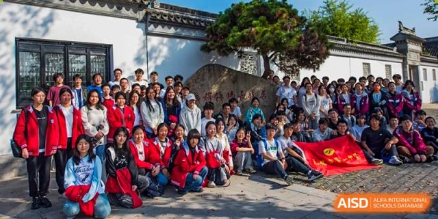 A large group of high school students sitting and posing for a group photo outdoors near a traditional rock feature at Wuxi No.1 High School.