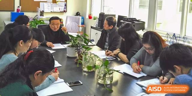 A group of adults or staff meeting around a table with potted plants in a conference room at Yang Guang Qing International School of Beijing.