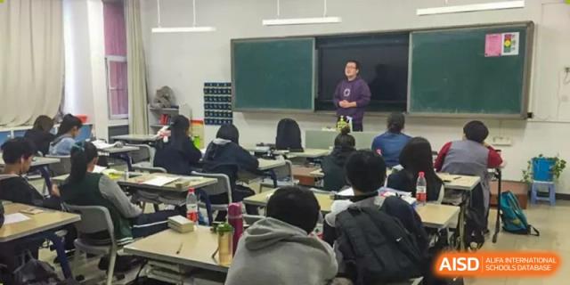 A teacher instructing students seated in a classroom with a green chalkboard in the background at Yang Guang Qing International School of Beijing.