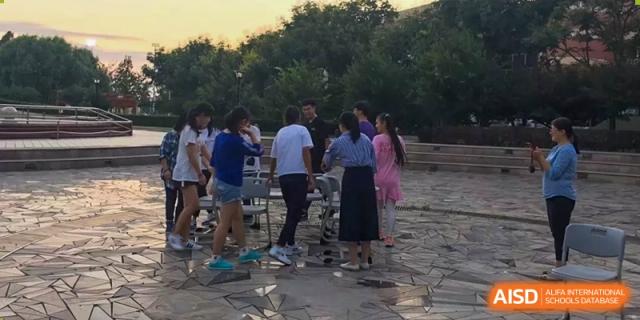 A small group of students standing and socializing in a park-like outdoor area at Yang Guang Qing International School of Beijing.