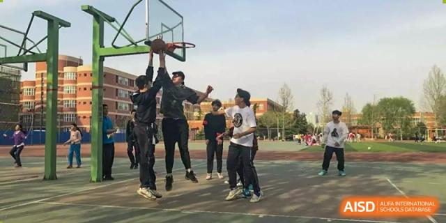 Students jumping and reaching for the basketball during a game on an outdoor court at Yang Guang Qing International School of Beijing.