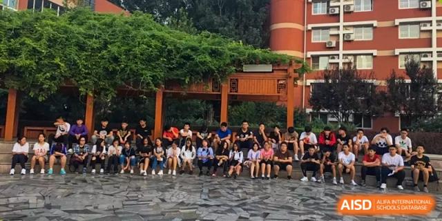 A group of students sitting together in a shaded, paved outdoor area on the school grounds at Yang Guang Qing International School of Beijing.