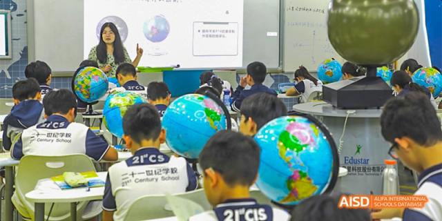 Students seated at desks in a classroom with two students in the foreground holding large inflatable globe balls, during a lesson, at 21ST Century School, Wenjiang, Chengdu.