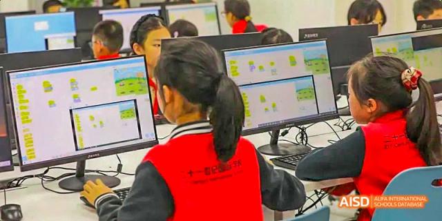 A student in a red vest concentrating while working on an interactive program on a desktop computer, during a technology class, at 21ST Century School, Wenjiang, Chengdu.