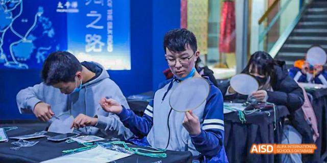 A male student in glasses and a uniform concentrating on a science experiment, holding a circular reflective plate, at 21ST Century School, Wenjiang, Chengdu.