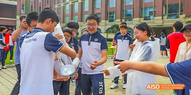 A group of male students laughing and interacting with a scientific device, possibly a spotlight or reflector, during an outdoor science activity, at 21ST Century School, Wenjiang, Chengdu.