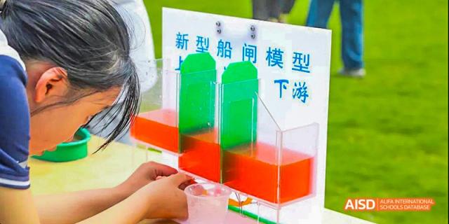 Hands demonstrating a physics or chemistry experiment with red and green liquids in clear acrylic containers, at 21ST Century School, Wenjiang, Chengdu.