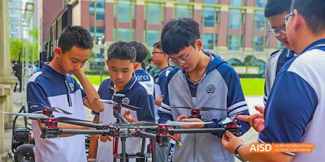 A group of male students examining and working on a drone for a technology or engineering project outdoors, at 21ST Century School, Wenjiang, Chengdu.
