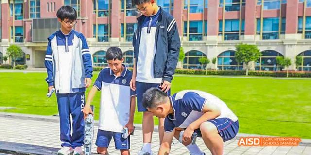 Students working on a hands-on project on the ground outdoors, with two male students in blue and white uniforms observing the activity, at 21ST Century School, Wenjiang, Chengdu.