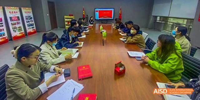 An indoor meeting or testing room with students seated at a long table, where an award certificate and red paper box are visible on the table, at 21ST Century School, Wenjiang, Chengdu.