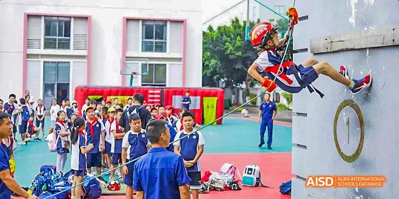 Students and teachers on a school playground, with a student wearing a red helmet preparing to jump, at 21ST Century School, Wenjiang, Chengdu.