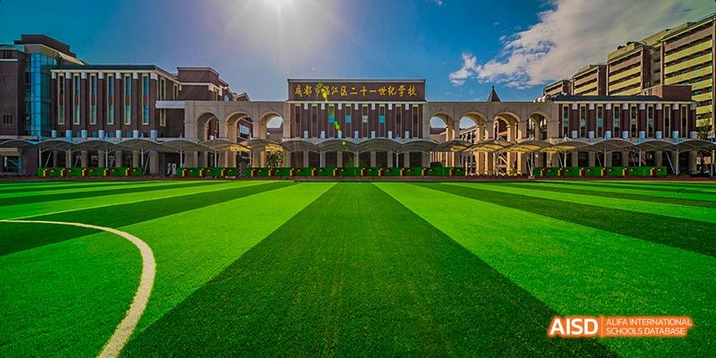 The main entrance and facade of a large school building overlooking a perfectly manicured green lawn, under a bright blue sky, at 21ST Century School, Wenjiang, Chengdu.