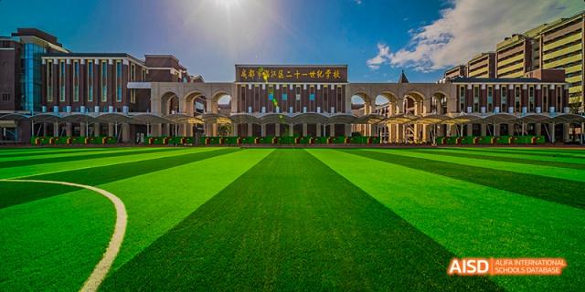 The main entrance and facade of a large school building overlooking a perfectly manicured green lawn, under a bright blue sky, at 21ST Century School, Wenjiang, Chengdu.
