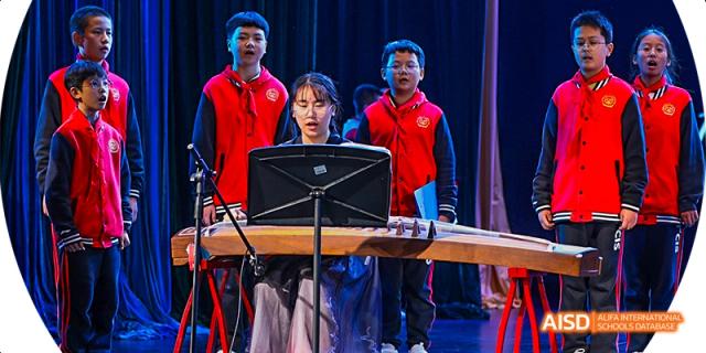 A female student playing a traditional Chinese musical instrument while other students in red vests watch, during a school performance, at 21ST Century School, Wenjiang, Chengdu.