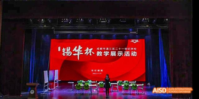 An indoor stage decorated with red banners featuring Chinese text, likely for a teacher demonstration or performance event, at 21ST Century School, Wenjiang, Chengdu.