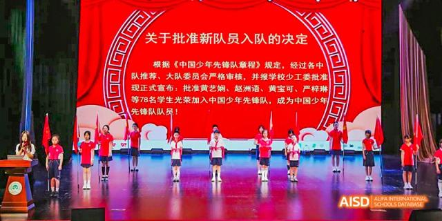 A stage banner with Chinese text and students performing a synchronized dance routine in red vests below it, during a school ceremony, at 21ST Century School, Wenjiang, Chengdu.