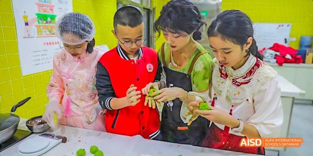 A female teacher or instructor helping a male student in a red vest prepare food during a hands-on cooking class, demonstrating practical life skills, at 21ST Century School, Wenjiang, Chengdu.
