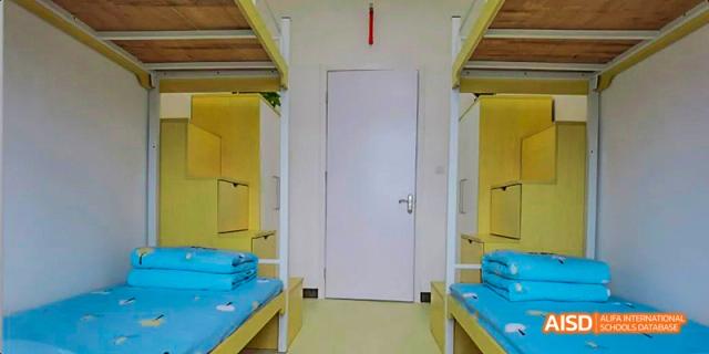 The interior of a student dormitory room, showing two sets of bunk beds and a closed door, highlighting the residential facilities, at 21ST Century School, Wenjiang, Chengdu.
