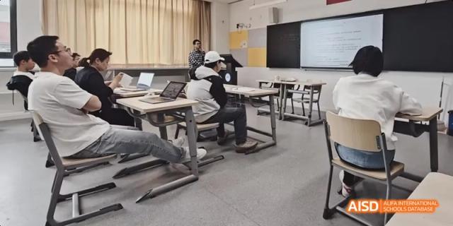 Students seated at desks with laptops, listening to a teacher lecture in a bright, modern classroom at BDA School of The High School Affiliated to Renmin University of China.