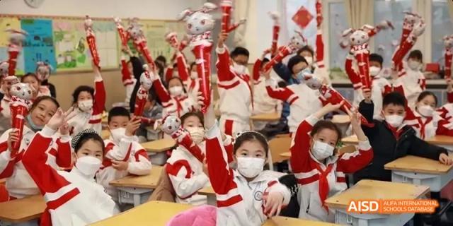 Students in a festive classroom cheering with their hands raised, many wearing masks, at BDA School of The High School Affiliated to Renmin University of China.