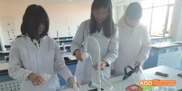 A student in a lab coat working on a physical science or engineering model constructed from white piping at BDA School of The High School Affiliated to Renmin University of China.