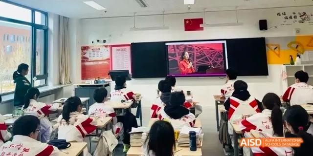 Students seated at desks watching a lecture or presentation being delivered remotely on a large screen in the classroom at BDA School of The High School Affiliated to Renmin University of China.