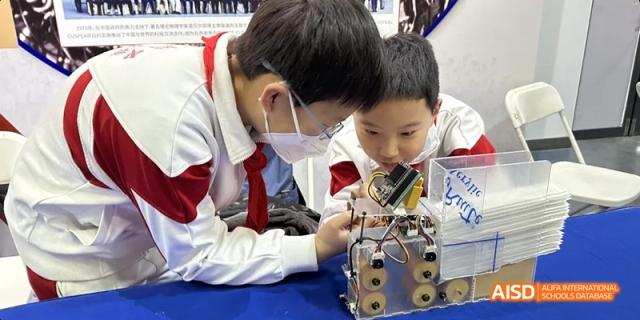 Two male students, one wearing a mask, working collaboratively to assemble or test a robot or mechanical device at BDA School of The High School Affiliated to Renmin University of China.