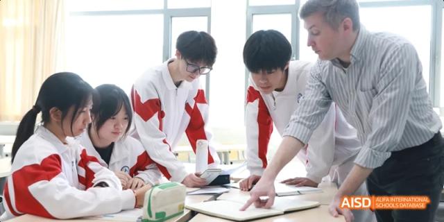 Two male students in red and white school vests collaborating on a design or planning activity over a paper on a desk at BDA School of The High School Affiliated to Renmin University of China.