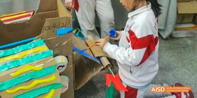 A close-up of students working together, assembling a cardboard and paper tube project with small flags at BDA School of The High School Affiliated to Renmin University of China.