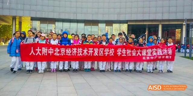 A large group of young students smiling and holding a banner outdoors at BDA School of The High School Affiliated to Renmin University of China.