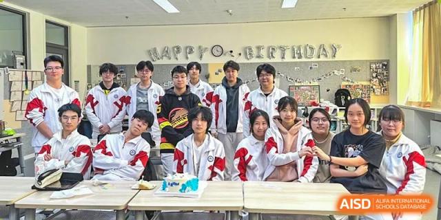 A group of students posing around a table with a cake, celebrating a birthday or event at BDA School of The High School Affiliated to Renmin University of China.
