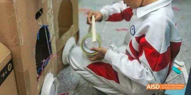 A close-up of a student in a red and white uniform carefully applying gold tape to a craft project at BDA School of The High School Affiliated to Renmin University of China.