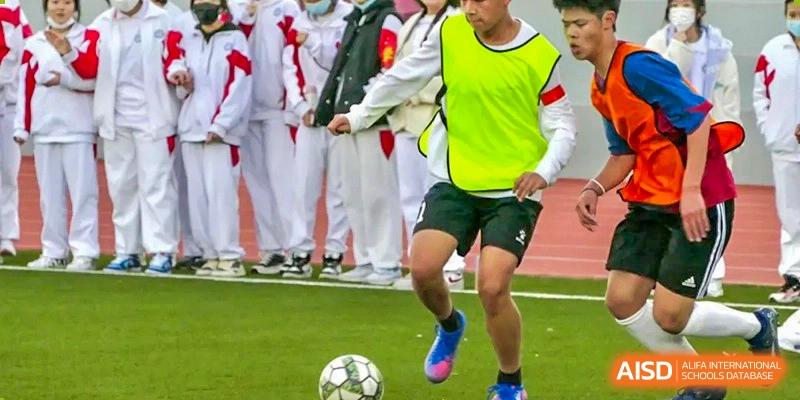 A close-up of a student in a bright green vest playing soccer on a grass field at BDA School of The High School Affiliated to Renmin University of China.