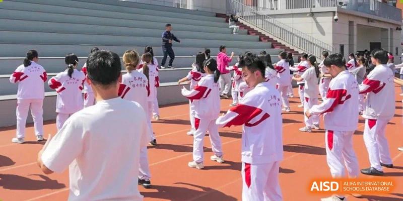 Students in white and red uniforms participating in an outdoor physical activity or warm-up on the red track at BDA School of The High School Affiliated to Renmin University of China.