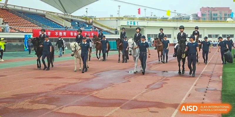 Students and staff leading horses during an equestrian event or lesson near a sports track at BDA School of The High School Affiliated to Renmin University of China.