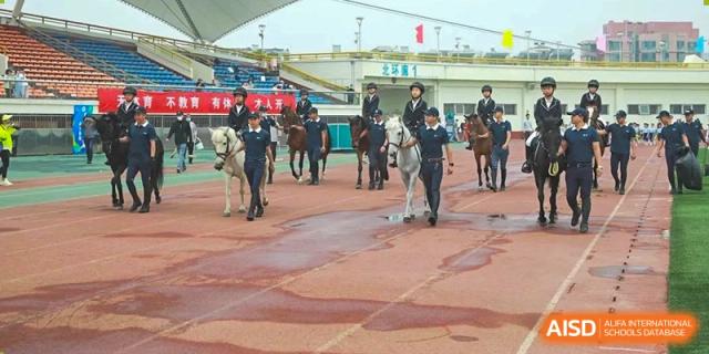 Students and staff leading horses during an equestrian event or lesson near a sports track at BDA School of The High School Affiliated to Renmin University of China.