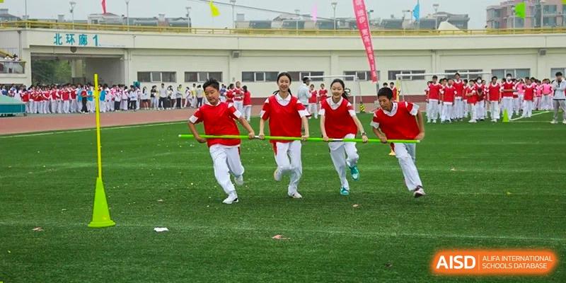 Students in red and white uniforms running a relay or sprint race on an outdoor track at BDA School of The High School Affiliated to Renmin University of China.