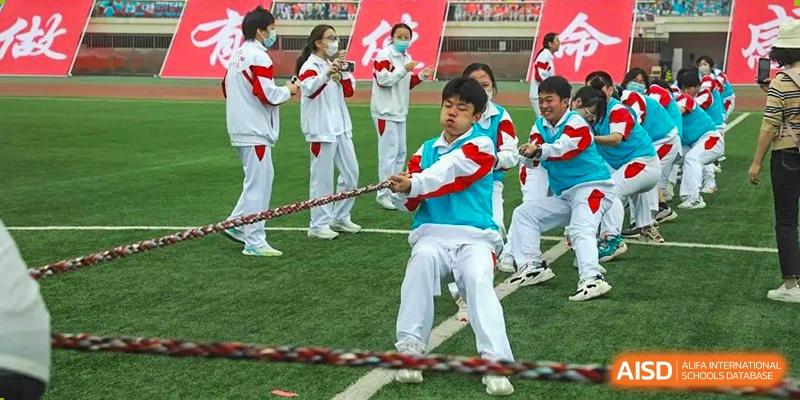 A student pulling a rope during a vigorous tug-of-war competition on a grass field at BDA School of The High School Affiliated to Renmin University of China.
