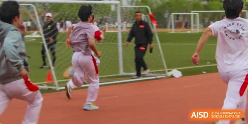 A student in a red and white uniform running near a soccer goal on a track with a coach or staff member nearby at BDA School of The High School Affiliated to Renmin University of China.