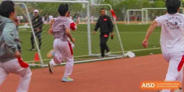 A student in a red and white uniform running near a soccer goal on a track with a coach or staff member nearby at BDA School of The High School Affiliated to Renmin University of China.