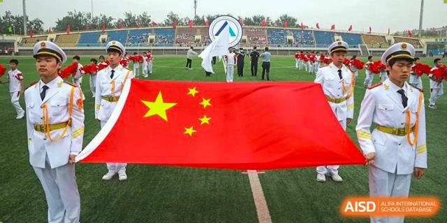A large Chinese flag being carried or displayed on the grass field during an opening ceremony or event at BDA School of The High School Affiliated to Renmin University of China.