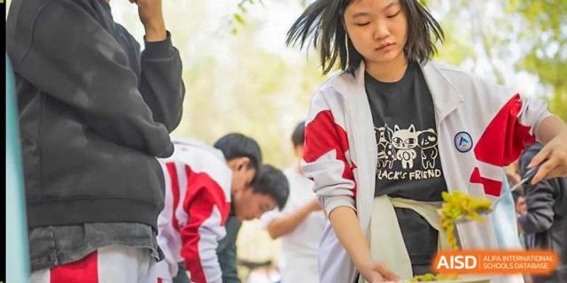 Students in uniform at BDA School of The High School Affiliated to Renmin University of China engaged in an outdoor activity, with one student bowing or bending over.
