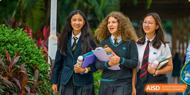 Two female students from The British School of Guangzhou in uniform, standing and discussing papers or homework they are holding.