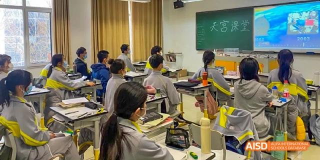 Students from Beijing No.2 Middle School sitting at their desks, wearing masks, and focused on a lesson in a bright classroom.