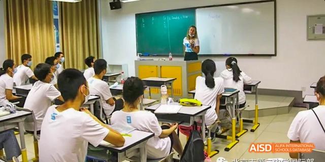 A teacher instructs students from Beijing No.2 Middle School in a classroom, standing in front of a green chalkboard.