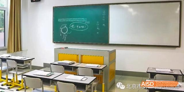 A clean classroom setting at Beijing No.2 Middle School with a green chalkboard, two yellow and grey desks, and a drawing of a smiling face.